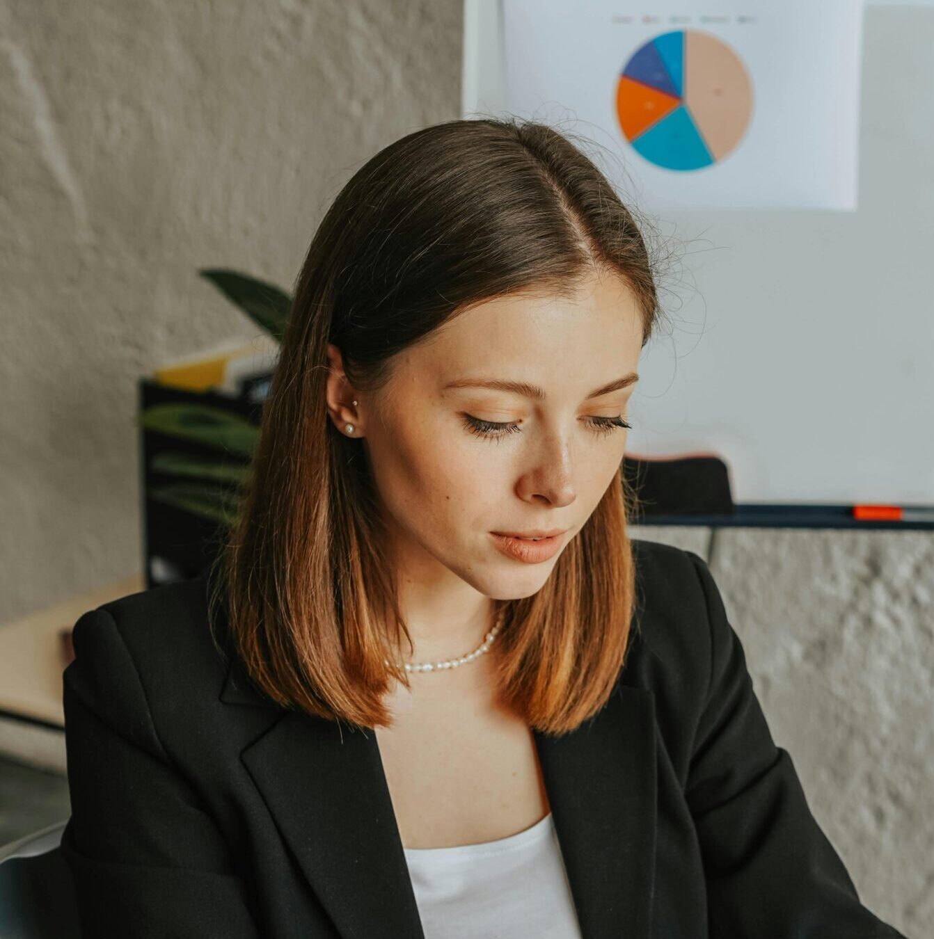 Confident businesswoman working on a laptop in a modern office environment with charts in the background.